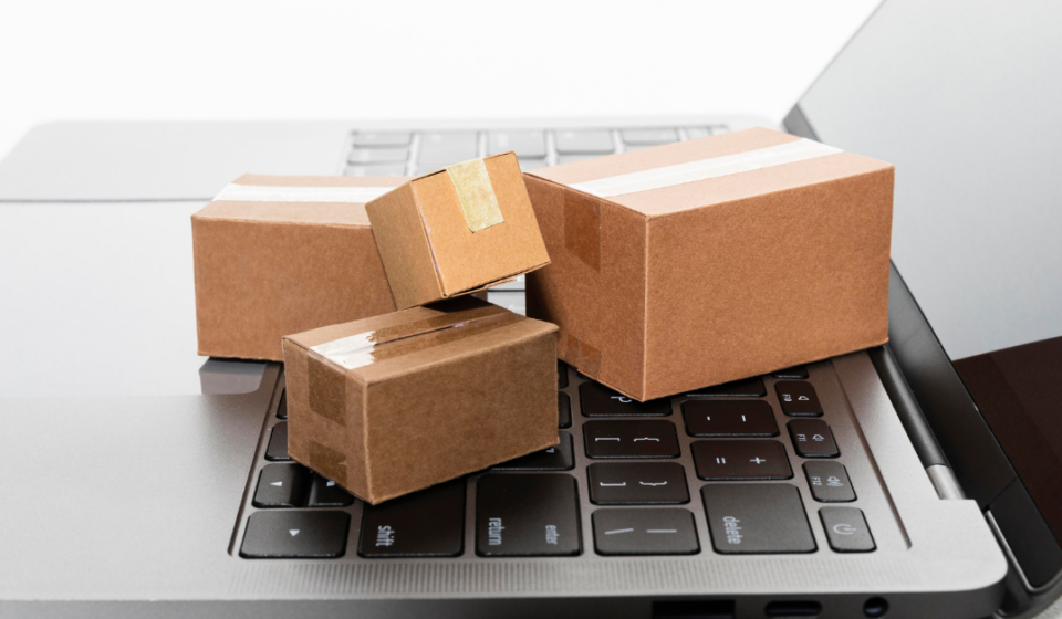 Four small cardboard packages placed on a laptop keyboard, representing logistics and procurement.